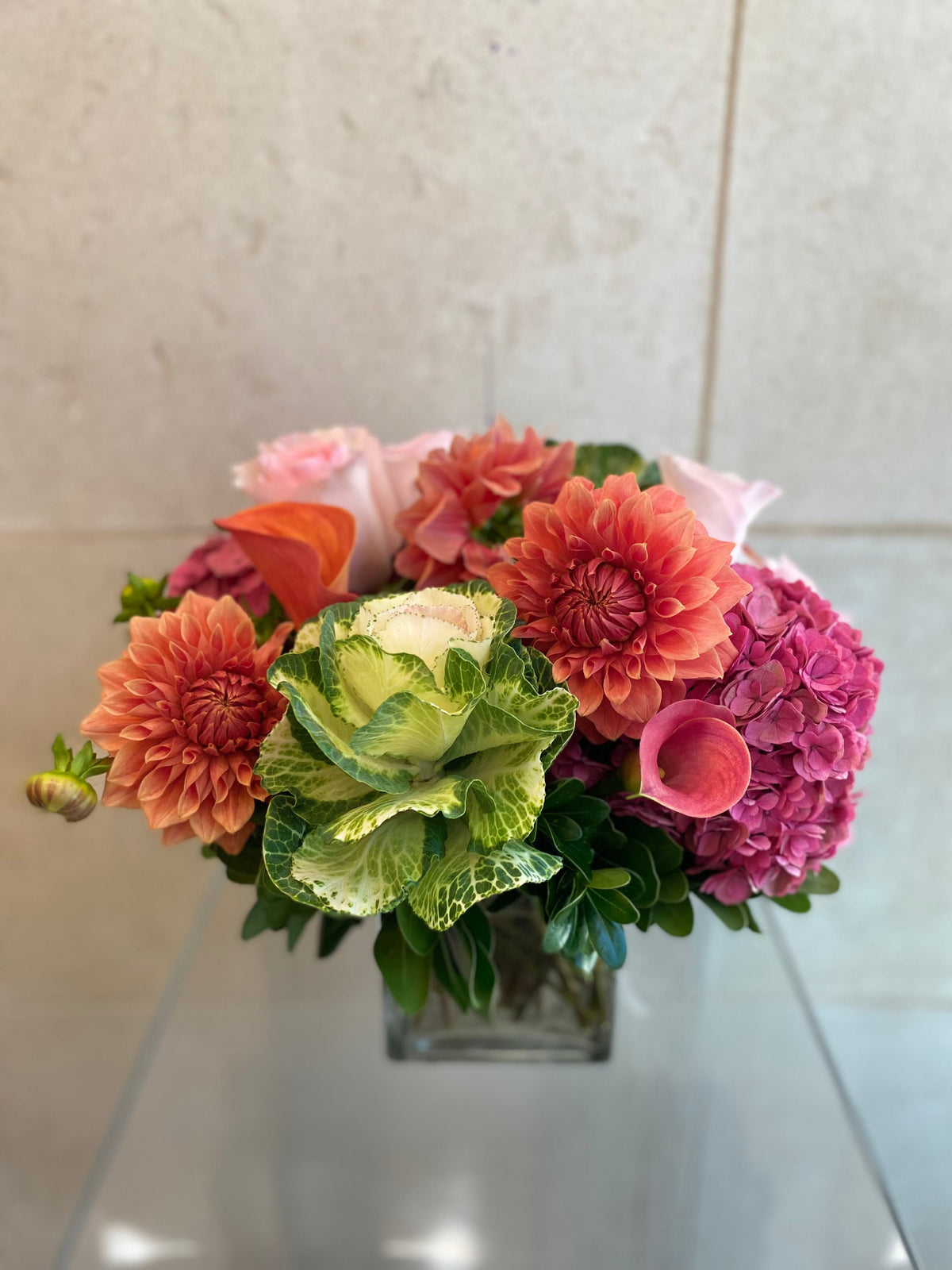 Autumn floral arrangement with dahlias, hydrangeas, calla lilies, and ornamental kale in warm pink and coral tones.