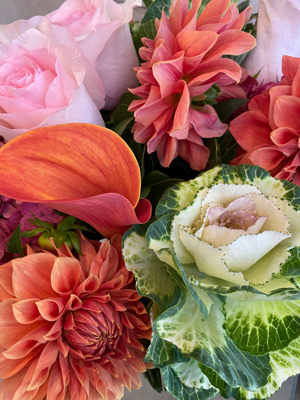 Autumn floral arrangement with dahlias, hydrangeas, calla lilies, and ornamental kale in warm pink and coral tones.