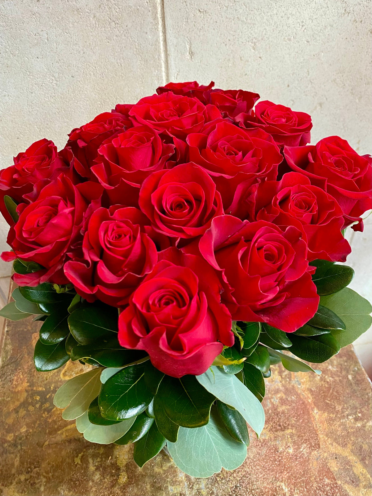 Red Freedom roses arranged in a leaf-lined glass cube vase with fresh greenery.