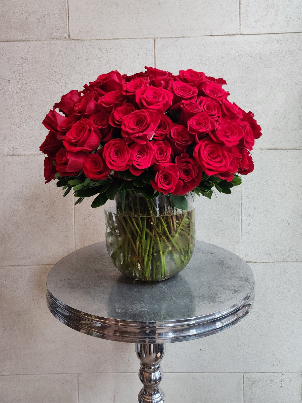 Large pavé arrangement of over 100 red roses with fresh greenery in a clear glass vase.