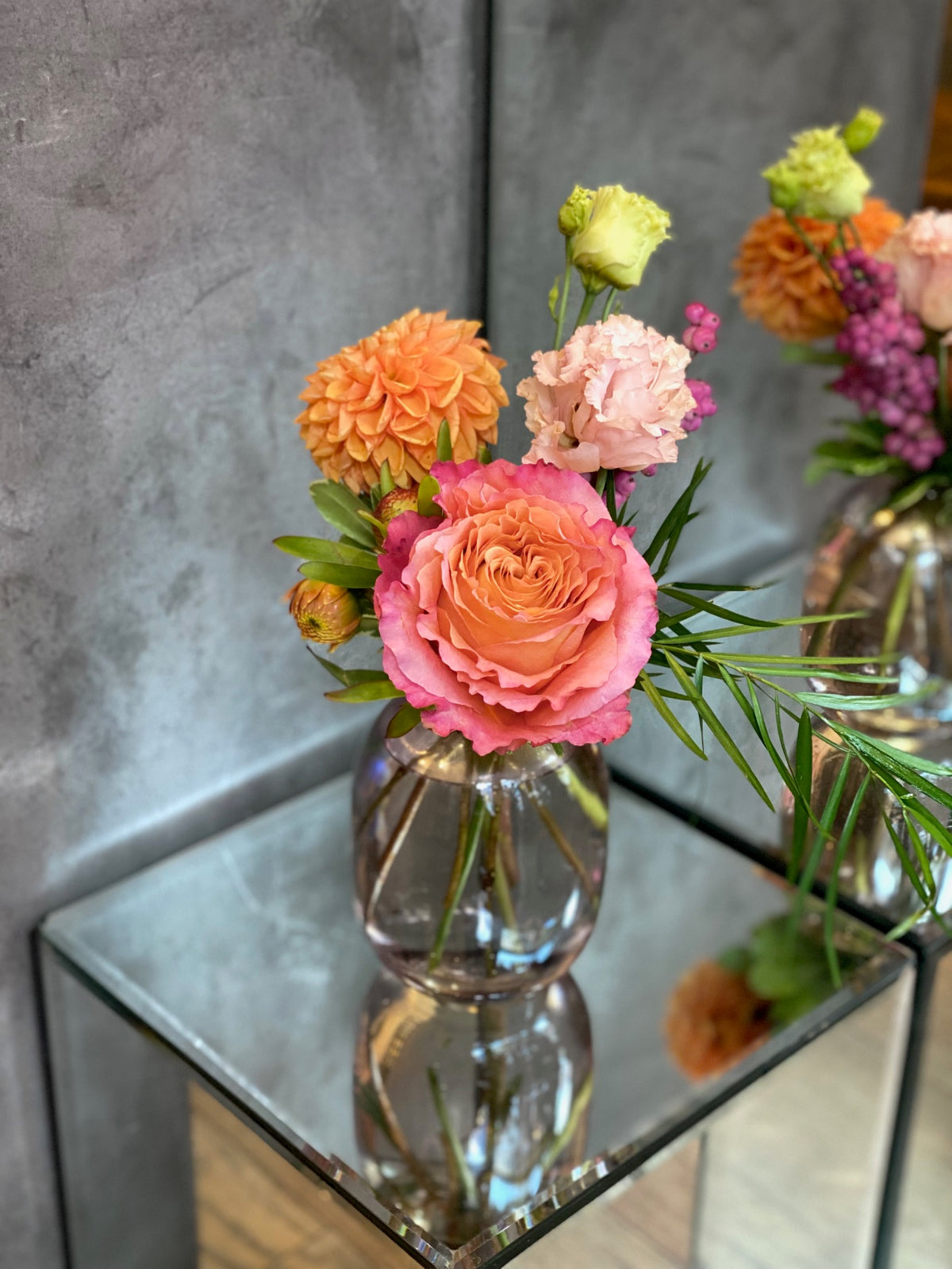 Set of three glass bud vases with seasonal flowers and greenery in warm autumn tones.
