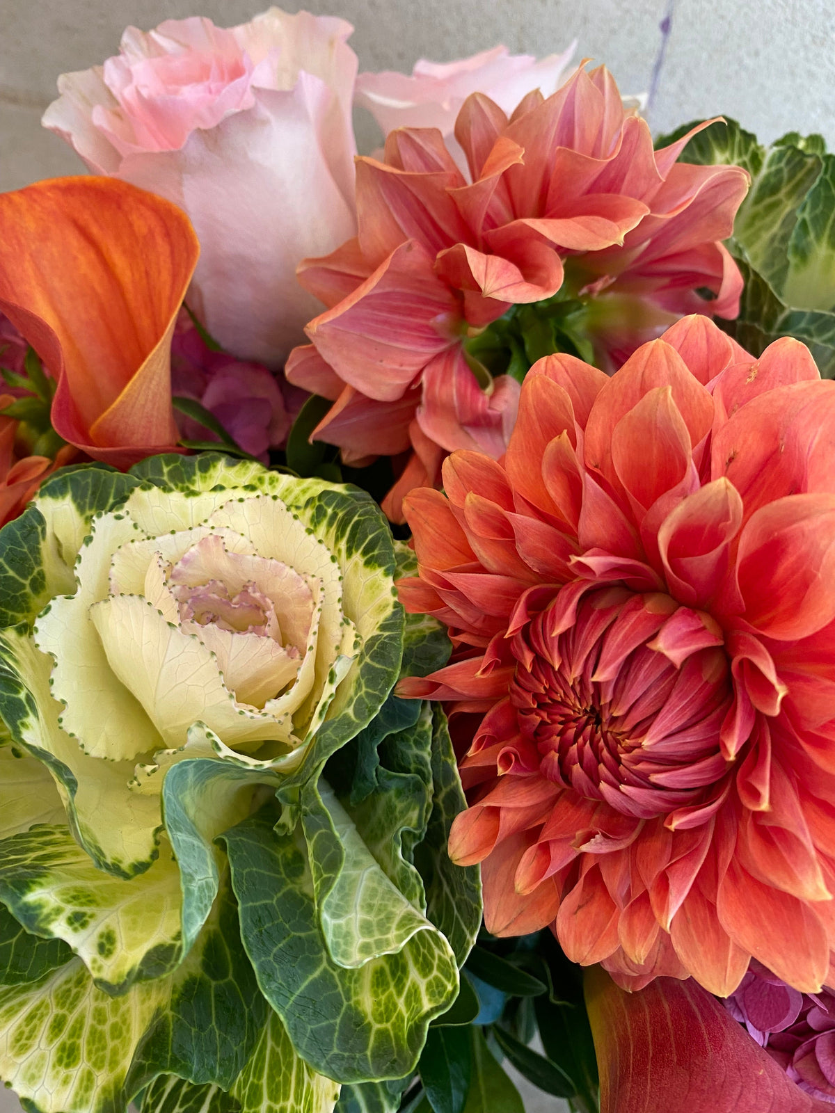 Autumn floral arrangement with dahlias, hydrangeas, calla lilies, and ornamental kale in warm pink and coral tones.