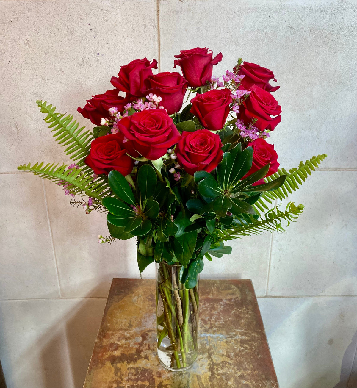 Dozen red roses with seasonal accent flowers and fresh greenery, available as a bouquet or vase arrangement.
