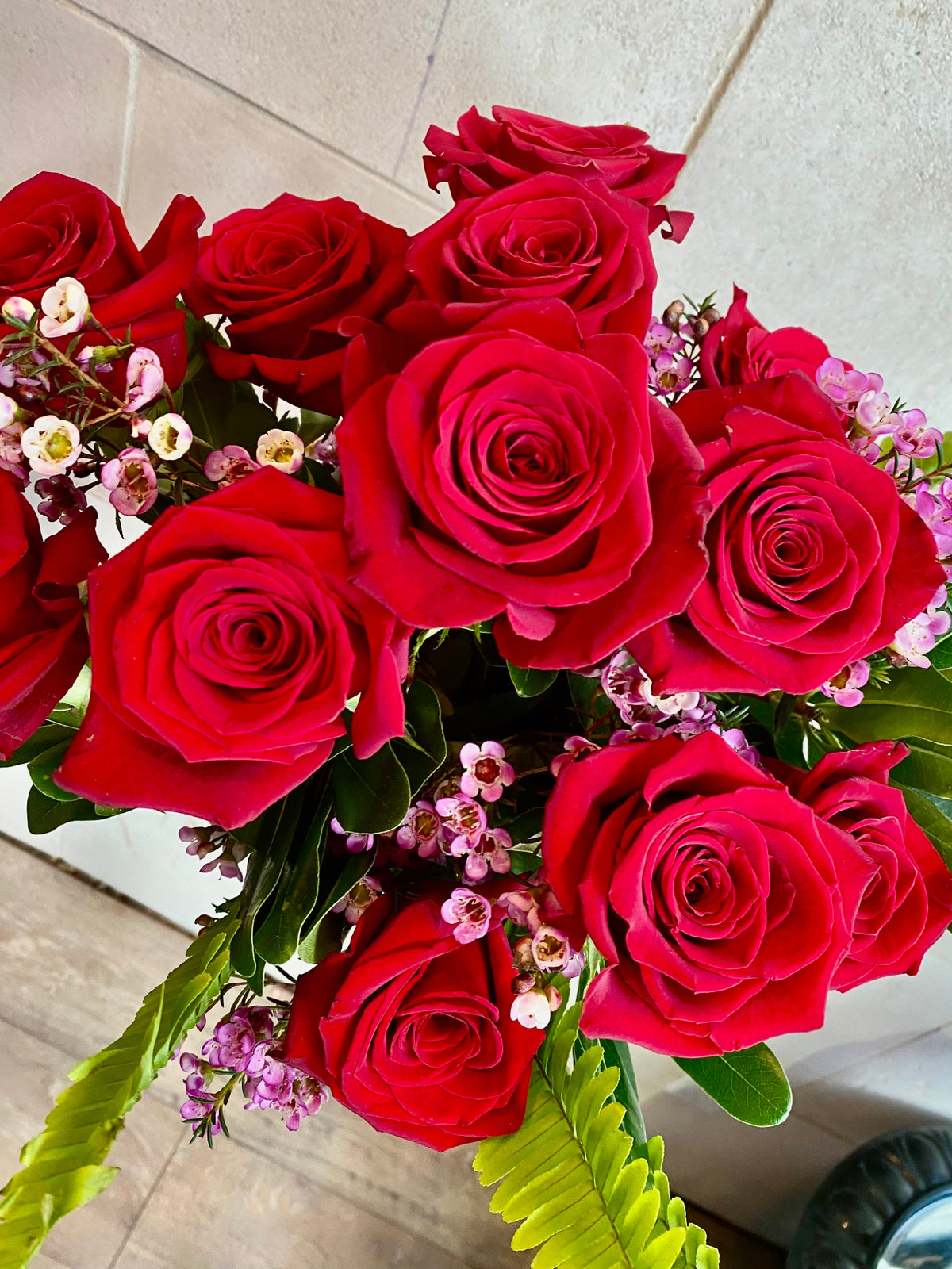 Dozen red roses with seasonal accent flowers and fresh greenery, available as a bouquet or vase arrangement.