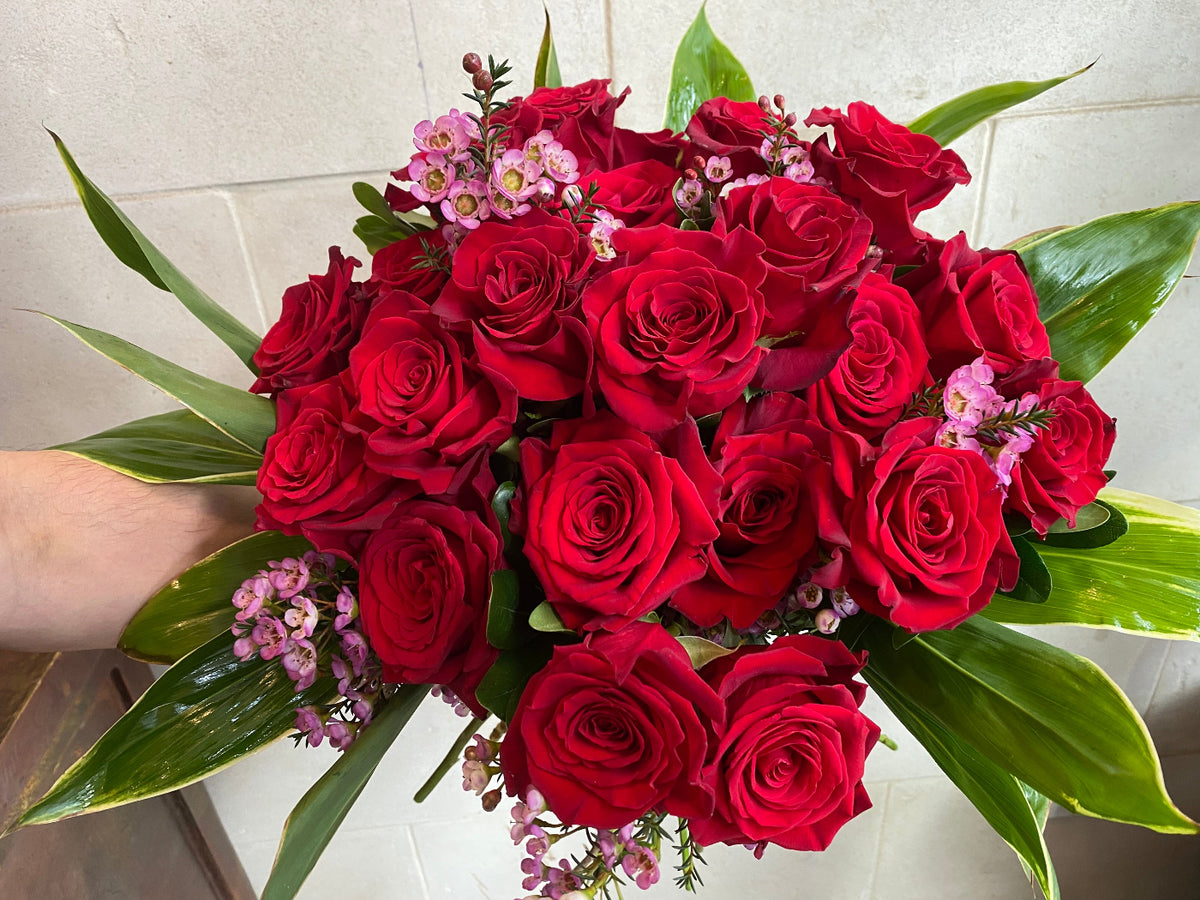 Dozen red roses with seasonal accent flowers and fresh greenery, available as a bouquet or vase arrangement.