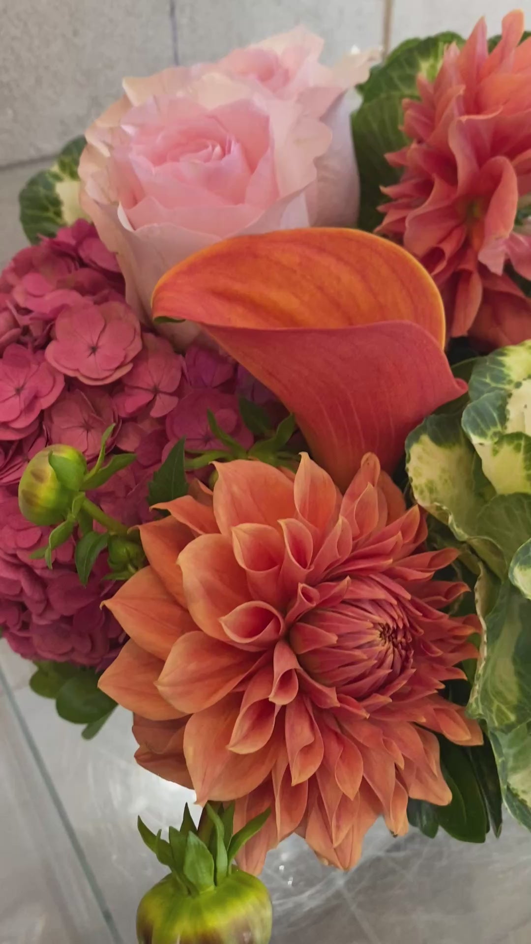 Autumn floral arrangement with dahlias, hydrangeas, calla lilies, and ornamental kale in warm pink and coral tones.