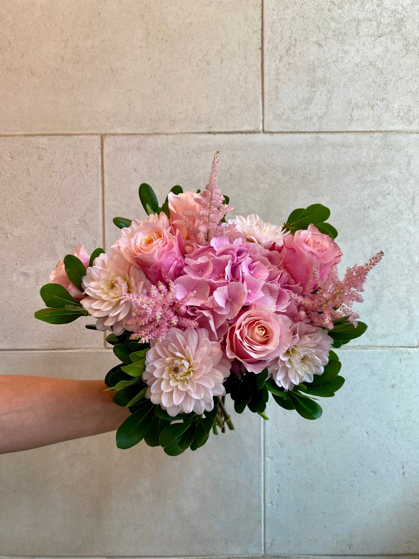 Hand-tied bouquet with pink hydrangeas, blush roses, dahlias, astilbe, and seasonal greenery.