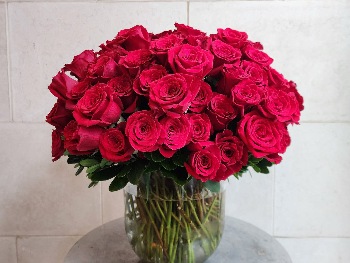 Large pavé arrangement of over 100 red roses with fresh greenery in a clear glass vase.