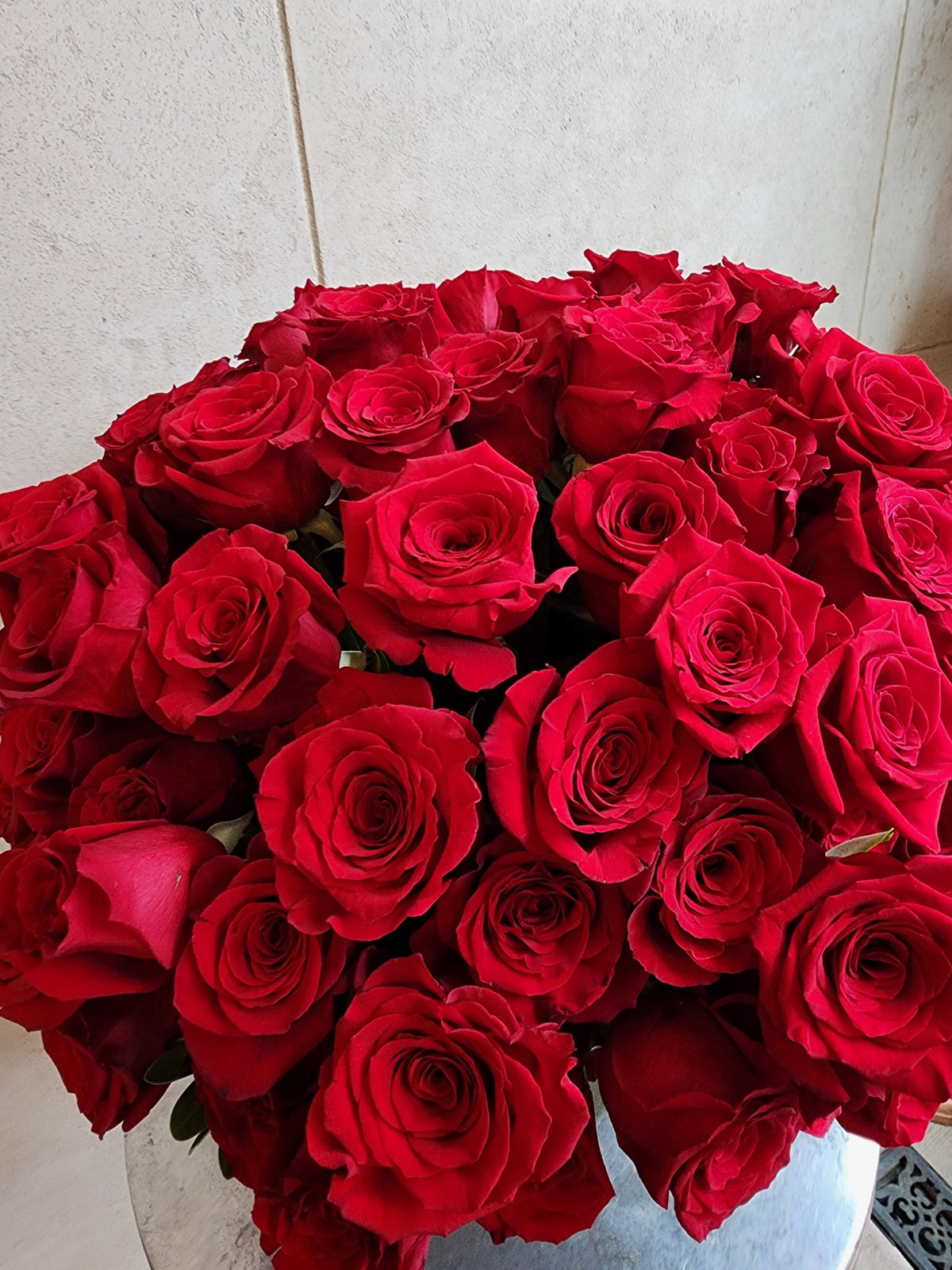 Large pavé arrangement of over 100 red roses with fresh greenery in a clear glass vase.